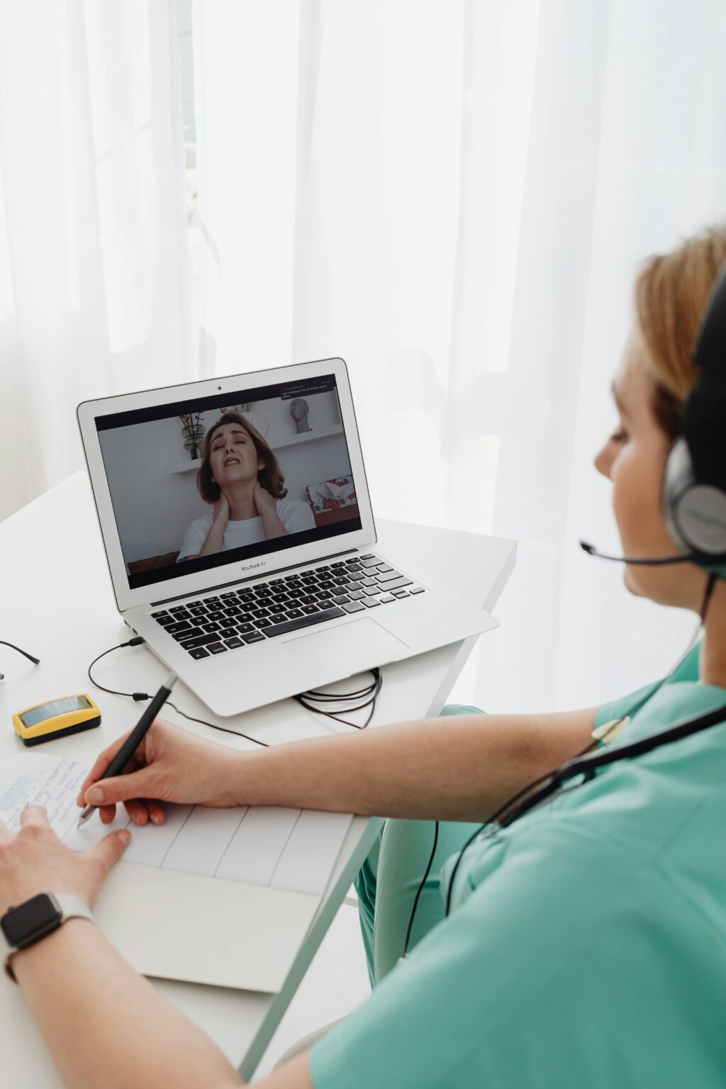 A doctor in scrubs conducting an online consultation via laptop.